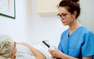 Close up of professional focused attractive nurse with eyeglasses sitting in front of woman patient with medications and clipboard at the hospital.