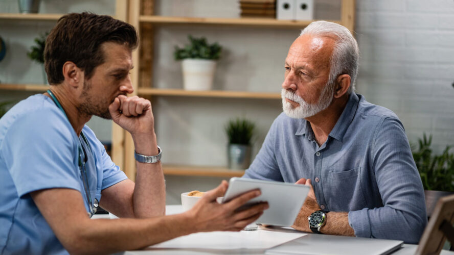 Senior man talking to a doctor who is using touchpad during medical appointment.