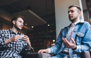 Young modern men talking together while drinking in cafe