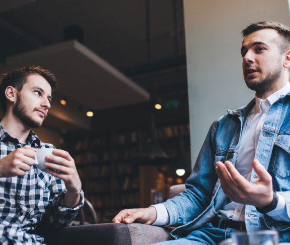 Young modern men talking together while drinking in cafe