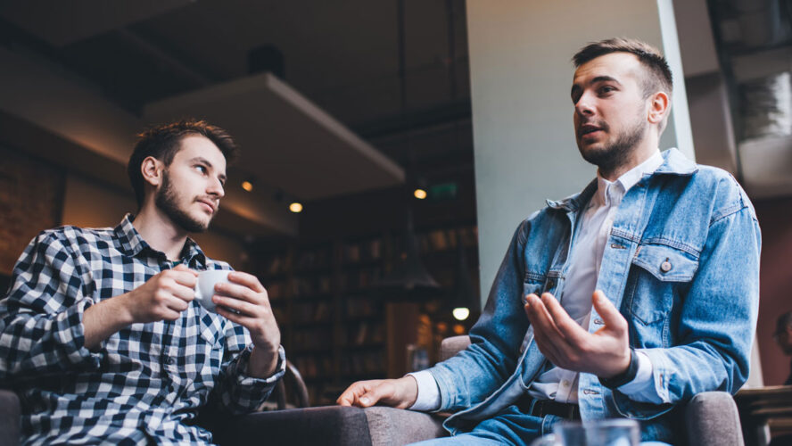 Young modern men talking together while drinking in cafe