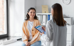 medicine, healthcare and people concept - female doctor with clipboard talking to smiling woman patient at hospital