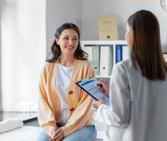medicine, healthcare and people concept - female doctor with clipboard talking to smiling woman patient at hospital