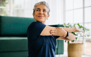 Happy and healthy senior woman doing a cross arm stretch in a peaceful yoga session at home
