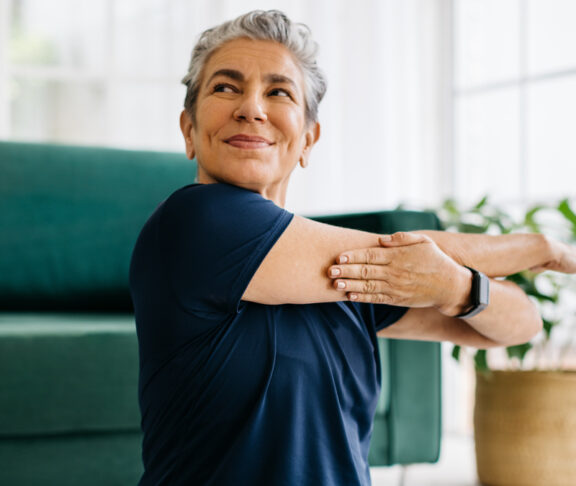 Happy and healthy senior woman doing a cross arm stretch in a peaceful yoga session at home