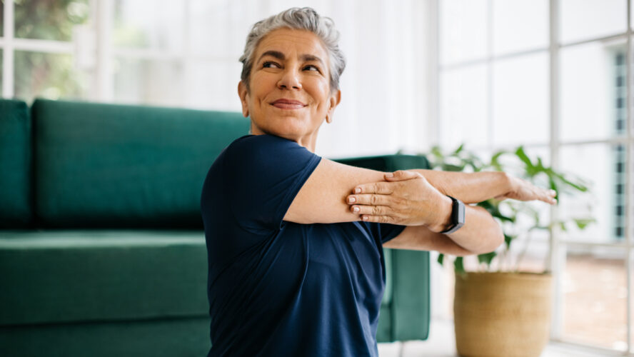 Happy and healthy senior woman doing a cross arm stretch in a peaceful yoga session at home