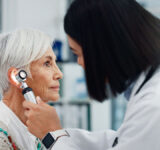 Senior woman, doctor and otoscope for ear, hearing test and exam, audio check or consultation for healthcare. Ent, otolaryngology and medical professional with elderly person for wellness in hospital