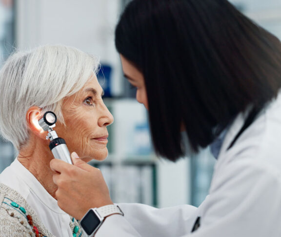 Senior woman, doctor and otoscope for ear, hearing test and exam, audio check or consultation for healthcare. Ent, otolaryngology and medical professional with elderly person for wellness in hospital
