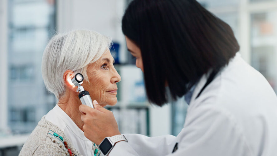 Senior woman, doctor and otoscope for ear, hearing test and exam, audio check or consultation for healthcare. Ent, otolaryngology and medical professional with elderly person for wellness in hospital