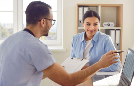 Medical consultation with male doctor, nurse in clinic, female patient visit. Physician showing laptop open screen, healthcare professional discussion for therapy, schedule arrangement to meet