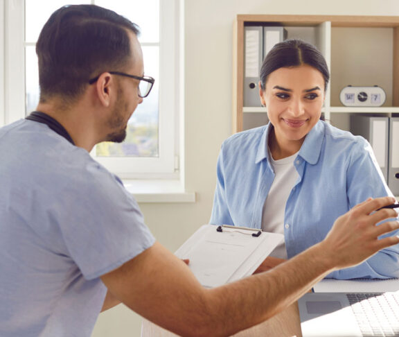 Medical consultation with male doctor, nurse in clinic, female patient visit. Physician showing laptop open screen, healthcare professional discussion for therapy, schedule arrangement to meet