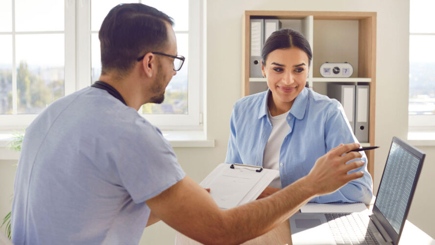 Medical consultation with male doctor, nurse in clinic, female patient visit. Physician showing laptop open screen, healthcare professional discussion for therapy, schedule arrangement to meet
