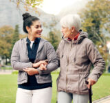 Senior woman, walker and nurse talking in a park with healthcare for elderly exercise. Walking, healthcare professional and female person with peace and physical therapy in a public garden with carer