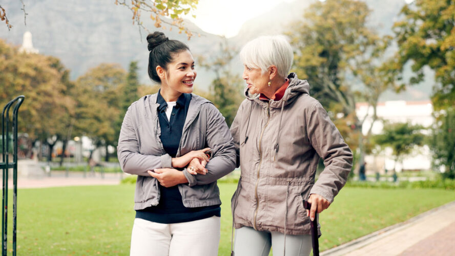 Senior woman, walker and nurse talking in a park with healthcare for elderly exercise. Walking, healthcare professional and female person with peace and physical therapy in a public garden with carer