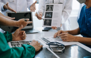 Medical team having a meeting with doctors in white lab coats and surgical scrubs seated at a table discussing a patients working online using computers in medical industry
