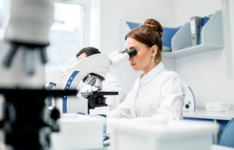 Young female medic in uniform working with microscope making analysis at the laboratory office