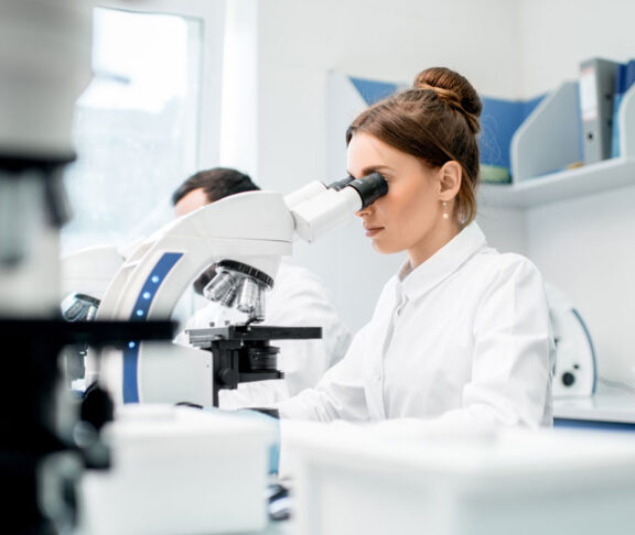 Young female medic in uniform working with microscope making analysis at the laboratory office