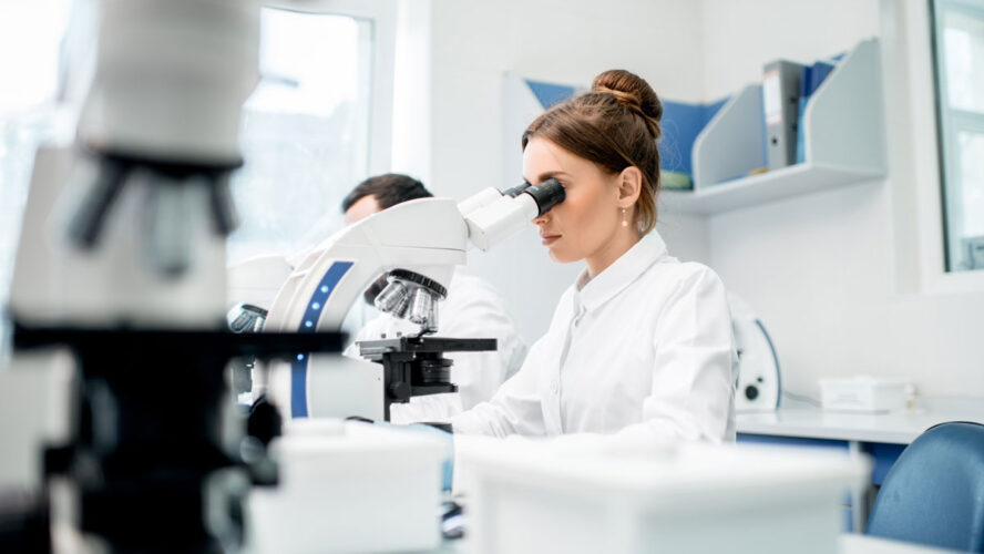 Young female medic in uniform working with microscope making analysis at the laboratory office
