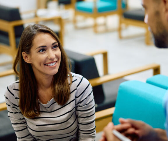 Happy woman talking to medical technician in waiting room at clinic