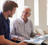 Senior man sitting looking at photo album with male nurse