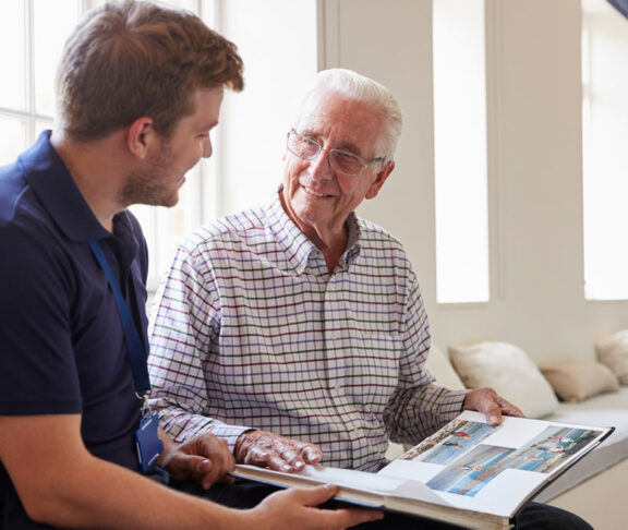 Senior man sitting looking at photo album with male nurse