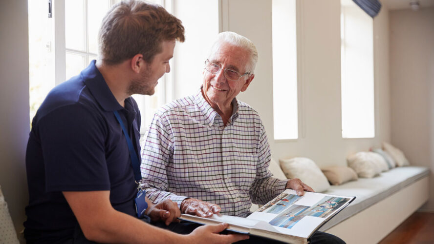 Senior man sitting looking at photo album with male nurse