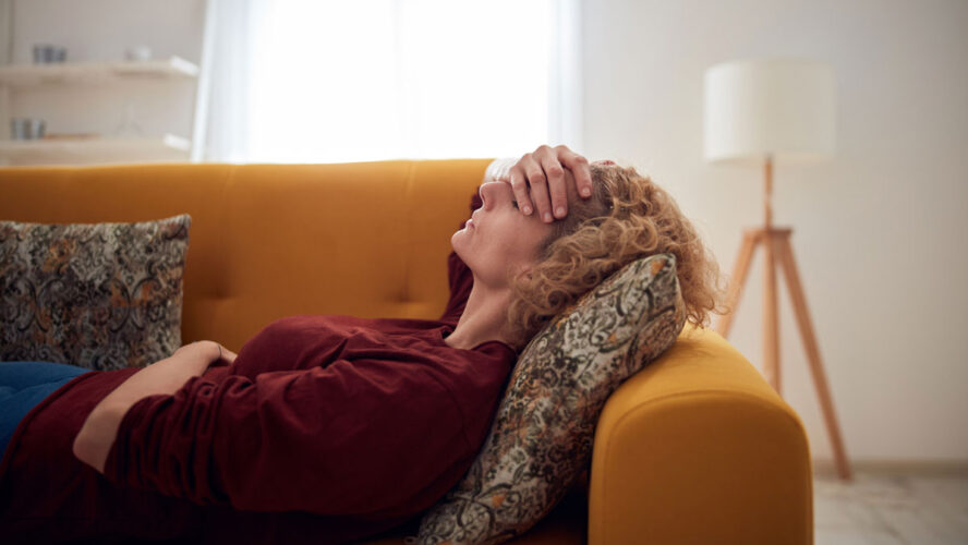 Woman with sinus pain, headache and stomach problems, lying on a couch at home