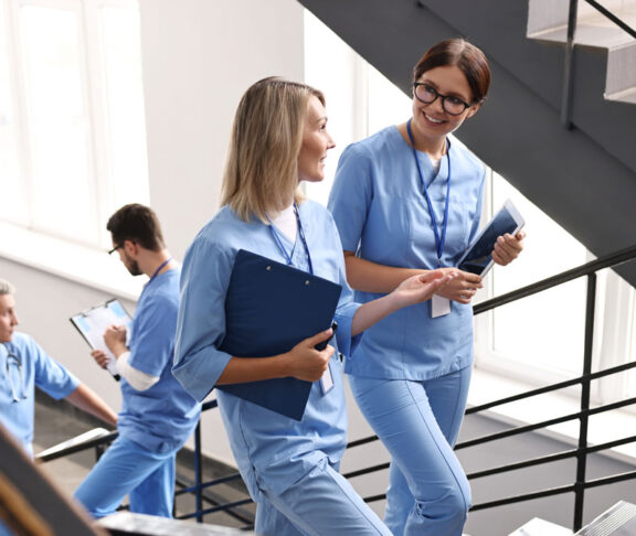 Healthcare workers with tablet and clipboard walking up stairs in hospital