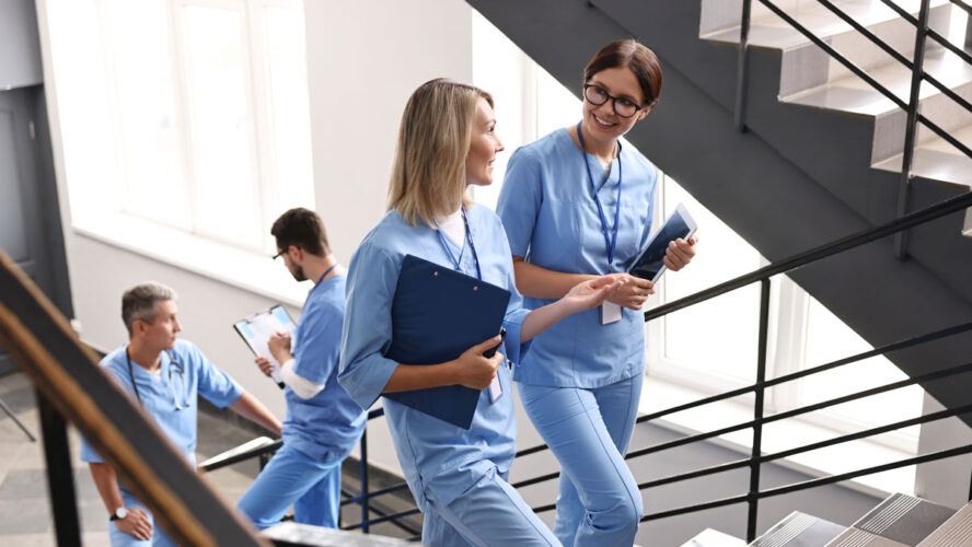 Healthcare workers with tablet and clipboard walking up stairs in hospital
