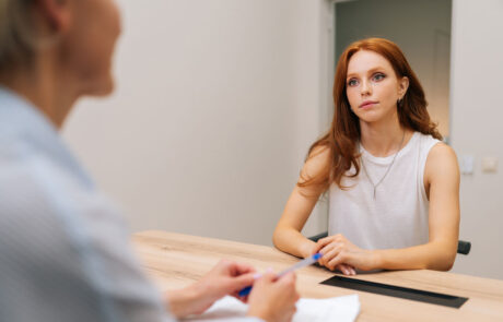 Over shoulder portrait of anxious woman patient listening attentively at medical consultation in modern office. Worried female patient discussing clinical result at healthcare appointment.