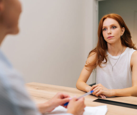 Over shoulder portrait of anxious woman patient listening attentively at medical consultation in modern office. Worried female patient discussing clinical result at healthcare appointment.