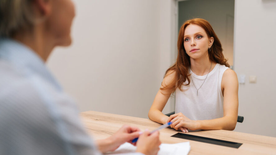 Over shoulder portrait of anxious woman patient listening attentively at medical consultation in modern office. Worried female patient discussing clinical result at healthcare appointment.