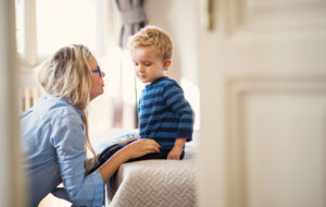 A young mother talking to her toddler son inside in a bedroom.