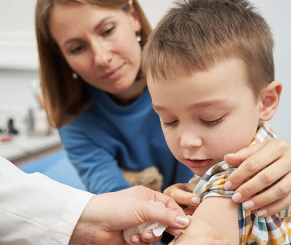 Doctor placing medical plaster on child arm after vaccination