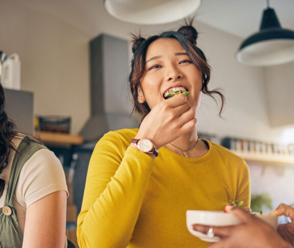 Women, friends and eating healthy food in home for bonding, nutrition and happy lunch together. Fruit diet, sharing and wellness, fresh summer friendship and girls in kitchen with smile at party.