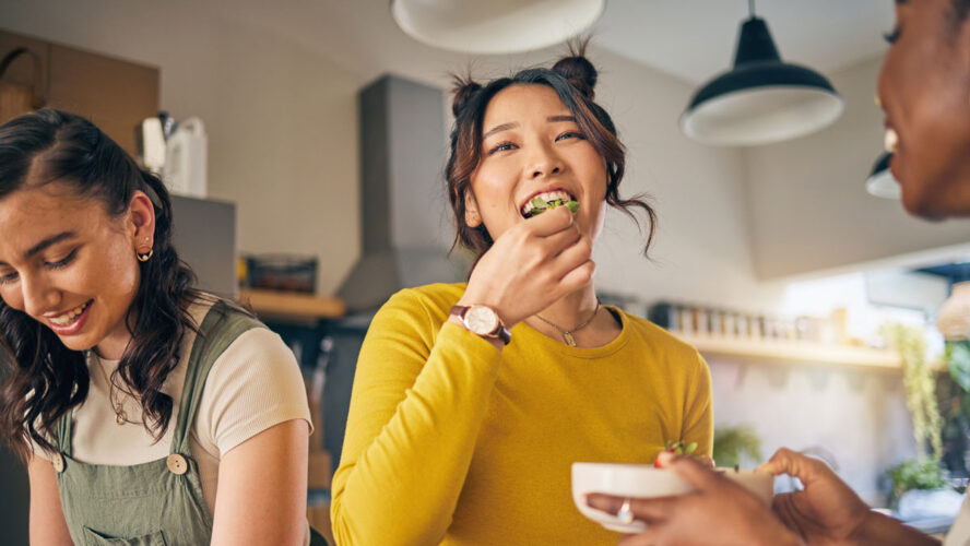 Women, friends and eating healthy food in home for bonding, nutrition and happy lunch together. Fruit diet, sharing and wellness, fresh summer friendship and girls in kitchen with smile at party.