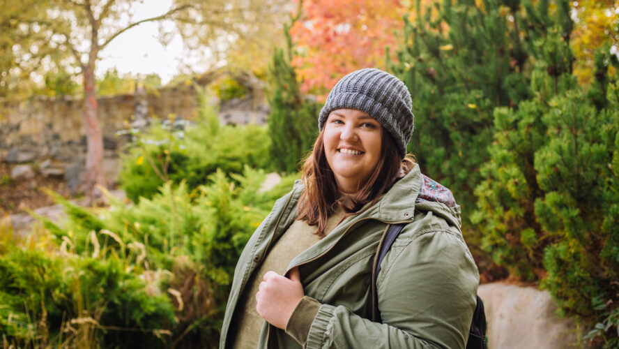 Young cheerful curvy woman in grey hat and green jacket walking in the park