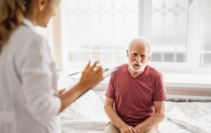Portrait of smiling patient describing his state of health while female physician listening and noting. Focus on bearded gentleman