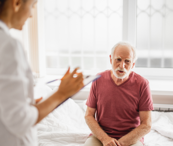 Portrait of smiling patient describing his state of health while female physician listening and noting. Focus on bearded gentleman