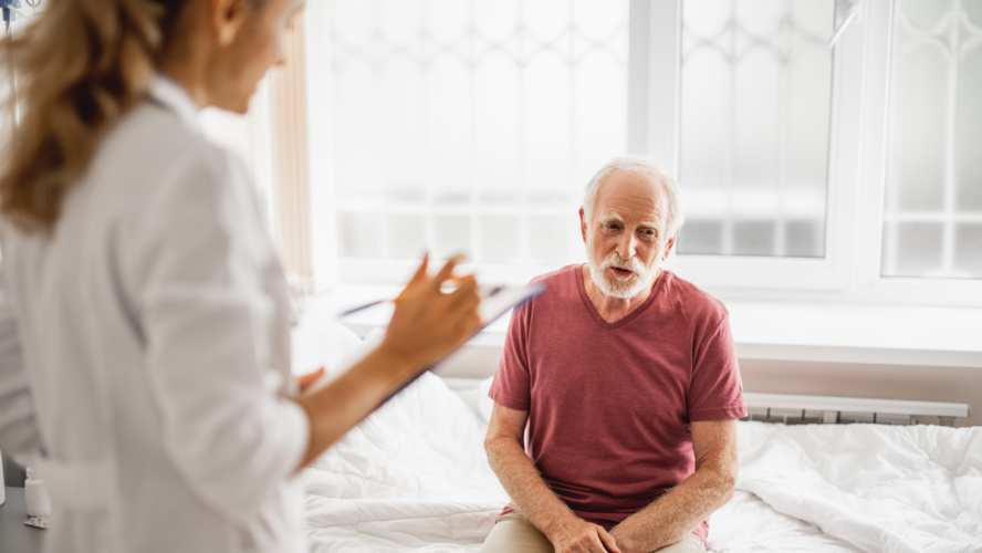 Portrait of smiling patient describing his state of health while female physician listening and noting. Focus on bearded gentleman