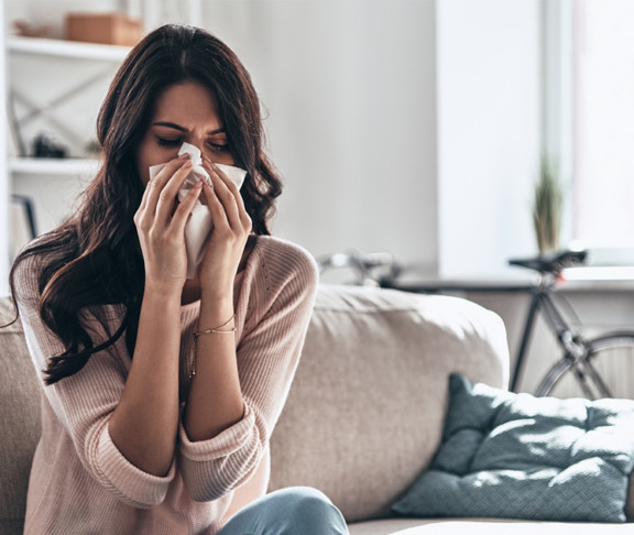 ick young woman blowing the nose using tissue paper while sitting on the sofa at home
