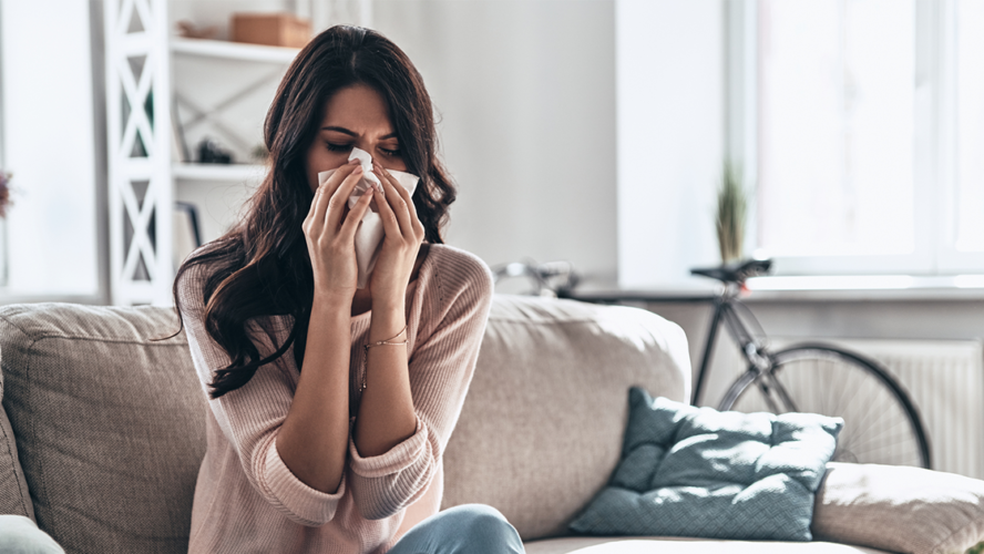 ick young woman blowing the nose using tissue paper while sitting on the sofa at home